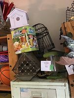 Photo showing white wooden birdhouse, boxed My Spy Birdhouse kit, metal grid bird feeder, and green plastic feeder on a white cabinet