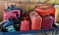 Four red fuel cans and three bottles of motor oil, assorted sizes and partially used.
