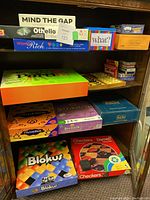 Shelf with multiple boxed board games including Mind the Gap, Othello, Word Rich, Partini, Scribblish, Encore, ThinkBlot, Blokus, Checkers, and Darwin Checkers.