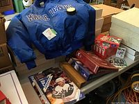 Photo showing blue Maple Leafs jacket on table with hockey card albums, magazines, and boxes of unopened 1972 Team Canada hockey cards stacked around.