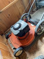View of the entire Husqvarna orange lawn mower showing front and back wheels, engine with pull start, and metal handlebar controls.