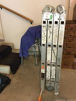 Four-section Krause conversion ladder folded and standing upright, showing heavy metal construction and some paint stains.