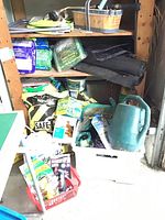 Wide shot of 3 shelves holding garden care items including landscape fabric rolls, fertilizer bags, seed packets, and watering cans.