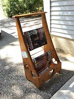 Front perspective view of the pine wood magazine holder showing magazines displayed on the horizontal spindles. Outdoor natural lighting highlights the wood grain and condition.