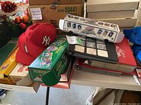 Photo showing various baseball card boxes, albums and two red baseball caps on table.