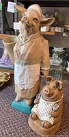 Photo showing both the tall pig figure and smaller pig figure together on a carpeted surface with background items including glass jars and shelves.