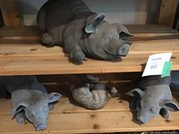 Four pig garden statues on wooden shelves: three resin pigs and one cement pig, varying sizes and poses.