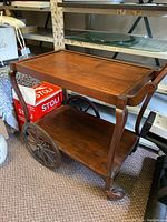 Full view of the wooden tea cart showing the large metal wheels and lower shelf.