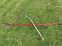 Full view of scythe lying on grass showing red handle and curved blade