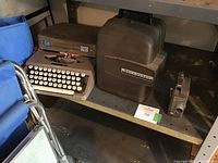 Wide shot showing the typewriter, projector, and camera arranged on a metal shelf.