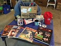 Full view of collection showing knit sweater, hat, mug, magazines, signed baseballs, and various memorabilia arranged on table.