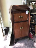 Front view of antique Victrola wooden cabinet showing double doors with ornate hardware and curved top design.
