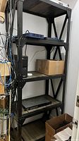 View of the shelving unit in a server room showing all five levels and some networking equipment and boxes stored on the shelves.