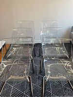 Front view of six transparent chairs on chrome frames arranged in two rows on patterned rug