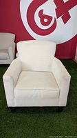Full front view of light grey upholstered armchair with square arms and cushioned seat, shown in a showroom