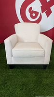 Front view of the light grey upholstered armchair showing seat cushion, backrest and armrests on green carpet background.