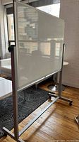 Full side view showing the whiteboard mounted on mobile aluminum frame with caster wheels inside an office space.