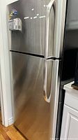 Angled front view of stainless steel refrigerator showing top freezer and bottom fridge doors with side handles.