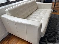Angled view of white leather loveseat showing tufted seat and back cushions and left side arm
