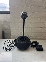Front view of Logitech BCC950 ConferenceCam showing the camera on a flexible neck attached to a round speaker base with cables and power adapter.