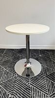 Full view of the round white adjustable bar table on a patterned carpet.