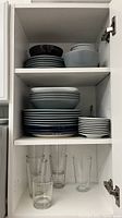 Open kitchen cabinet showing stacked ceramic plates and bowls of different sizes and colors on two shelves