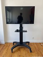 Front view of Panasonic Viera TV mounted on the Kanto TV cart with visible remote and power cable on the shelf.