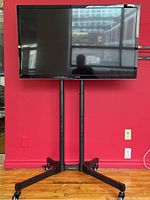 Front view of Panasonic Viera TV mounted on PrimeCables mobile TV cart against a red wall.