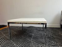 Front view of square white marble coffee table with chrome legs sitting on geometric patterned rug.