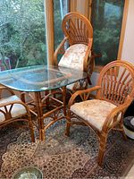 Dining set with bamboo frame table and four matching bamboo chairs with floral seat cushions by window on patterned rug.