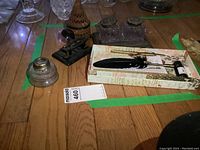 Overview of calligraphy and related items on wooden floor including glass ink jars in metal tray, woven straw trinket box, and vintage hole punch.