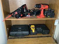 Photo showing the Power Max drill, Jobmate reciprocating saw with batteries and blades, and two black cases on wooden shelves.