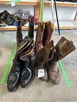 Four pairs of well-worn cowboy boots with various colors and stitching patterns, arranged on garage floor.
