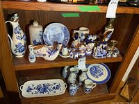 Photo showing two shelves filled with various Delft Blue Ware including pitchers, plates, vases, salt and pepper shakers, steins and trays.