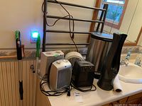 Photo showing four electric heaters, metal garbage pail, electric towel warmer on bathroom counter near a towel rack.