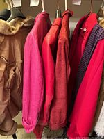 Side view of five jackets hanging in closet including red suede and red leather jackets close together.