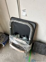 Full view of the folded platform hand truck with handle wrapped in bubble wrap, plastic packaging still around the base, casters visible beneath