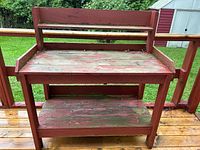 Front view showing the two-tier wooden potting table with weathered red paint, worn wood surface, and small back shelf.