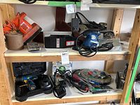 Shelf view showing various power tools including the orange corded belt sander, palm/detail sander, sandpaper rolls, cordless drill in case with charger and battery, screwdrivers, rotary tool kits, and walkie talkie.