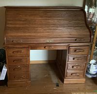 Full front view of the solid oak roll top desk with closed tambour top and multiple drawers.