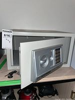 Front and open view of the electronic safe showing keypad, keyhole, round handle, and empty interior.