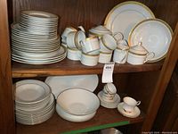 Full view of two shelves showing stacked dinner plates, cups, saucers, cream and sugar set, teapot, and various serving bowls.