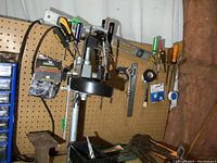 View of hand drill stand, railroad track anvil and tools mounted on pegboard.
