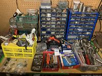 Overview of three hardware organizers filled with screws, nails, and small parts, yellow bin with cords, cordless driver, and various hand tools in plastic bins