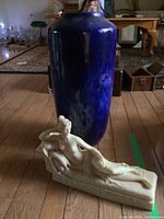 Front view of blue pottery vase and alabaster statuette on wooden floor showing overall condition and scale