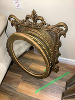 Photo showing stacked vintage mirrors and oval frame, capturing detailed ornate gold frames and visible wear