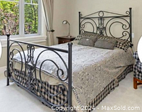 Full view of the black wrought iron queen size bedframe with headboard and footboard, bed skirt, and pillows arranged on the bed.