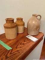 Photo showing two antique crocks and a stoneware jug on a wooden surface.