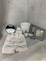 Overview of all bathroom items showing magnifying mirror, waste basket, framed wall mirrors, towels, soap dispenser, soap dish, and tissue box cover arranged on tiled surface