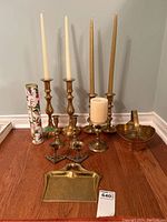 Full shot showing all brass items including dust pan, candle sticks, large candle holder, bucket, and match box arranged on floor.